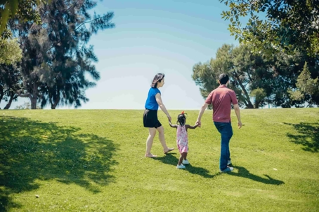 a woman and man holding a little girls hands while walking up a grassy hill